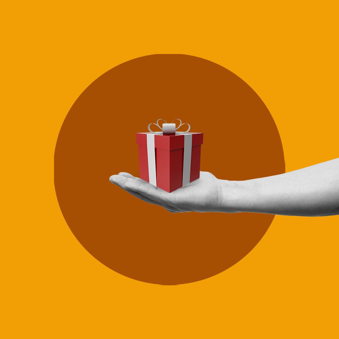 A hand holder a red gift box with a bow on top.